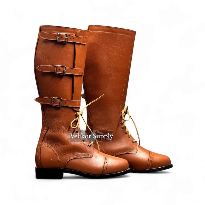 May include: A pair of brown leather riding boots. One boot features three buckle straps, while the other has laces. Both boots have a rounded toe and a small heel. The boots are set against a white background.