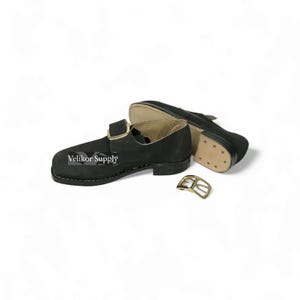 May include: Black leather shoes with a buckle closure and a gold-colored buckle. The shoes have a sturdy sole and are designed with a classic style. The text "Velikor Supply" is printed on the side of the shoe.