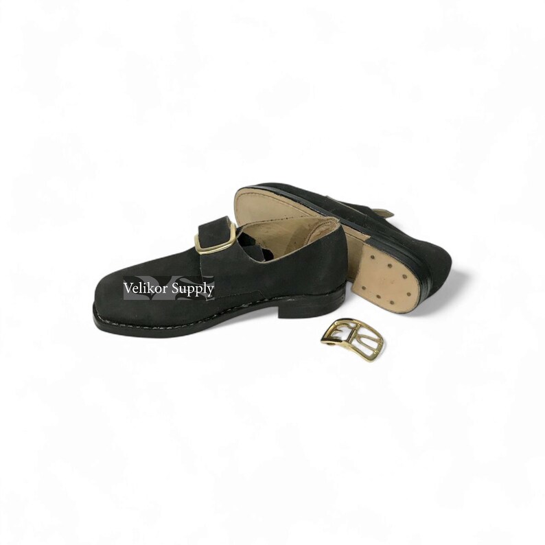 May include: Black leather shoes with a buckle closure and a gold-colored buckle. The shoes have a sturdy sole and are designed with a classic style. The text "Velikor Supply" is printed on the side of the shoe.