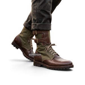 Op de afbeelding: Een paar veterschoenen van bruin leer en olijfgroen canvas met twee verstelbare banden met metalen gespen over de schacht. De laarzen hebben een rubberen profielzool en de tekst Velikor Supply is zichtbaar aan de zijkant.