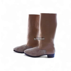 May include: A pair of tall, tan leather boots with a suede-like lower section. The boots have a knee-high design and a low heel. The text "Velikor Supply" is visible on the side of the boots.