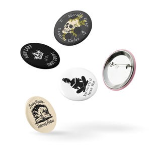 May include: A collection of five round and oval buttons with various designs and text. One button features a skull with floral accents and the text "Morally Gray is my Favorite Color." Other buttons include text like "High Lady of the Smut Court" and "Introverted Smut Slut."
