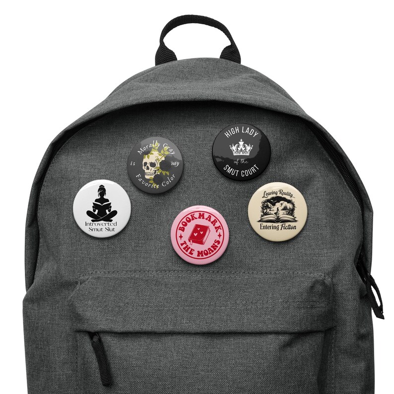 May include: A gray backpack with five round pinback buttons attached. The buttons feature various designs, including text and illustrations. One button reads "Morally Gray is my Favorite Color."