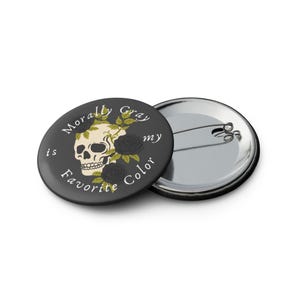 May include: A round, black button with the text "Morally Gray is my Favorite Color" encircling a skull and roses design. The skull is cream-colored, and the roses are black. A second button is visible.