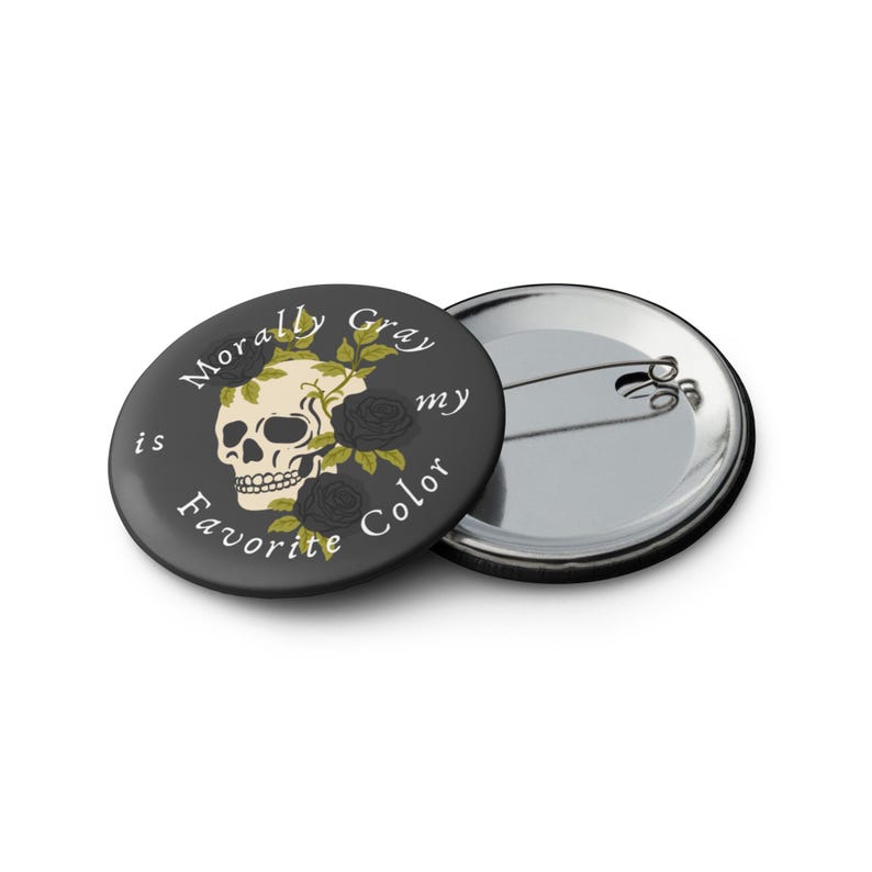 May include: A round, black button with the text "Morally Gray is my Favorite Color" encircling a skull and roses design. The skull is cream-colored, and the roses are black. A second button is visible.