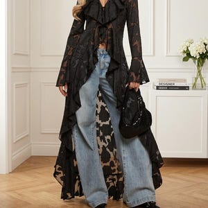 May include: A black sheer long-sleeved duster with a floral pattern, a deep V-neckline, and cascading ruffles along the front opening. The garment is paired with light blue wide-leg denim jeans and a black beaded handbag with a metallic finish.