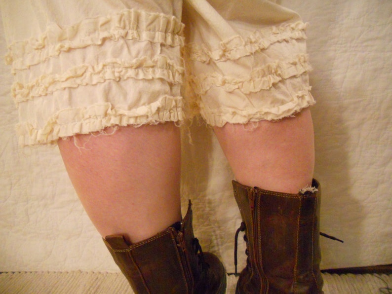 May include: White ruffled bloomers with brown leather boots. The boots have laces and a buckle.