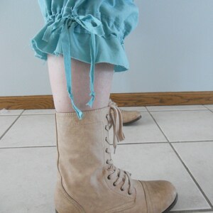 May include: A pair of tan lace-up boots with a rounded toe. The boots are worn with a light blue pair of pants with a gathered cuff.