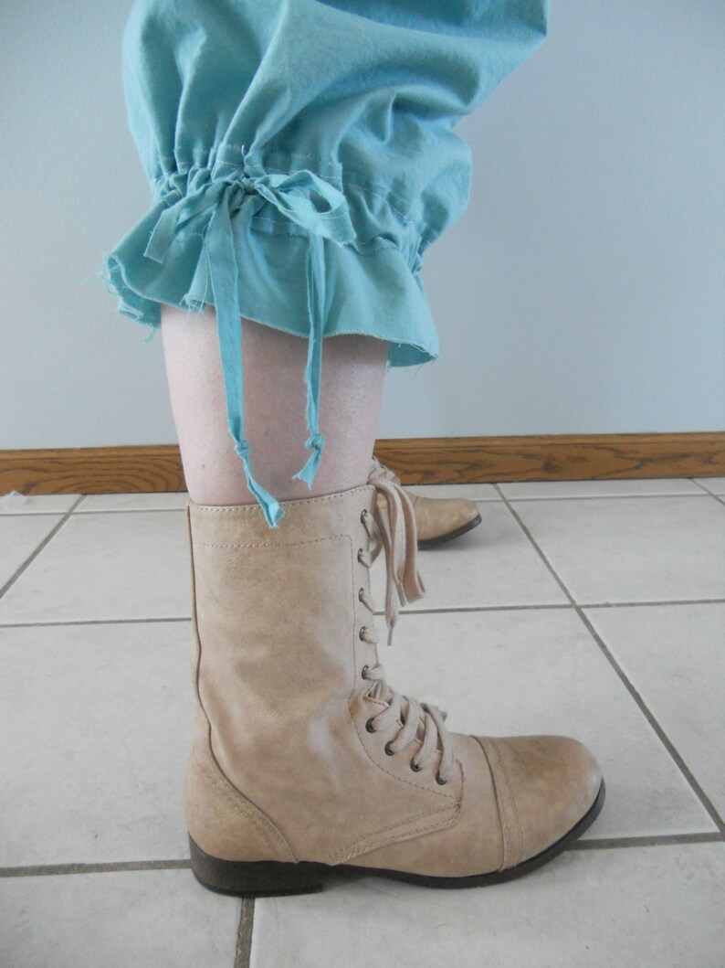 May include: A pair of tan lace-up boots with a rounded toe. The boots are worn with a light blue pair of pants with a gathered cuff.