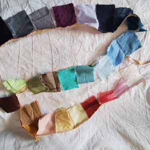 May include: A collection of fabric swatches in various colors and textures, arranged in a line on a white surface. The swatches are sewn together with a beige thread.