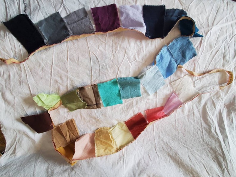 May include: A collection of fabric swatches in various colors and textures, arranged in a line on a white surface. The swatches are sewn together with a beige thread.