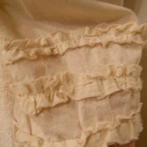 May include: A close-up of a white fabric with a ruffled trim. The fabric is soft and delicate, and the ruffles are evenly spaced.