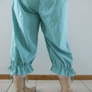 May include: A pair of light blue, gathered, cuffed pants with a ruffled hem. The pants are made of a soft, lightweight fabric and have a relaxed fit. The pants are worn with tan ankle boots.