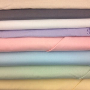 May include: A stack of eight fabric swatches in various pastel colors, including beige, gray, white, lavender, pink, light blue, green, and yellow. The swatches are labeled with names like "Tumble Weed", "Shadow", "Alabaster", "Mountain Bliss", "Prairie Rose", "Clear Blue Sky", "Spring", and "Sunshine".