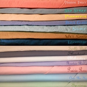 May include: A stack of 18 fabric swatches in various colors, including shades of blue, green, pink, and brown. The swatches are labeled with names like "Palm Leaf", "Passion Fruit", "Sea Spray", "Pineapple", "Beach Glass", "Surf", "Wet Sand", "Lagoon", "Tumble Weed", "Shadow", "Alabaster", "Mountain Bliss", "Prairie Rose", "Clear Blue Sky", "Spring", and "Sunshine".
