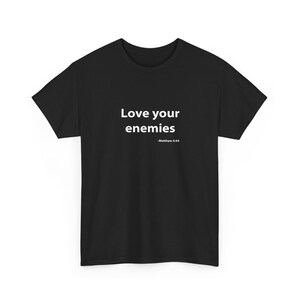 Może przedstawiać: Czarny t-shirt z białym napisem "Love your enemies" i odniesieniem "Mateusz 5:44". Koszulka ma okrągły dekolt.
