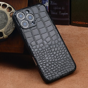 May include: Black phone case with a crocodile skin texture. The case has a glossy finish and features three camera lenses. The phone case is designed to protect the phone from scratches and damage.