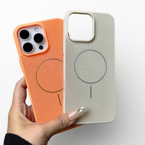 Puede incluir: Se muestran dos fundas para teléfono, una naranja y otra blanquecina. Las fundas tienen un diseño perforado con un patrón circular en el centro y un recorte para la cámara. La funda naranja tiene un borde naranja, mientras que la blanquecina tiene un borde blanco.