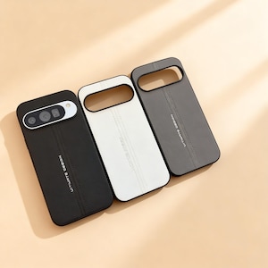 May include: Three phone cases in black, white, and grey. Each case has a stitched vertical line down the centre and the words "ULTIMATE DESIGN" printed vertically. The black case has a camera cutout.