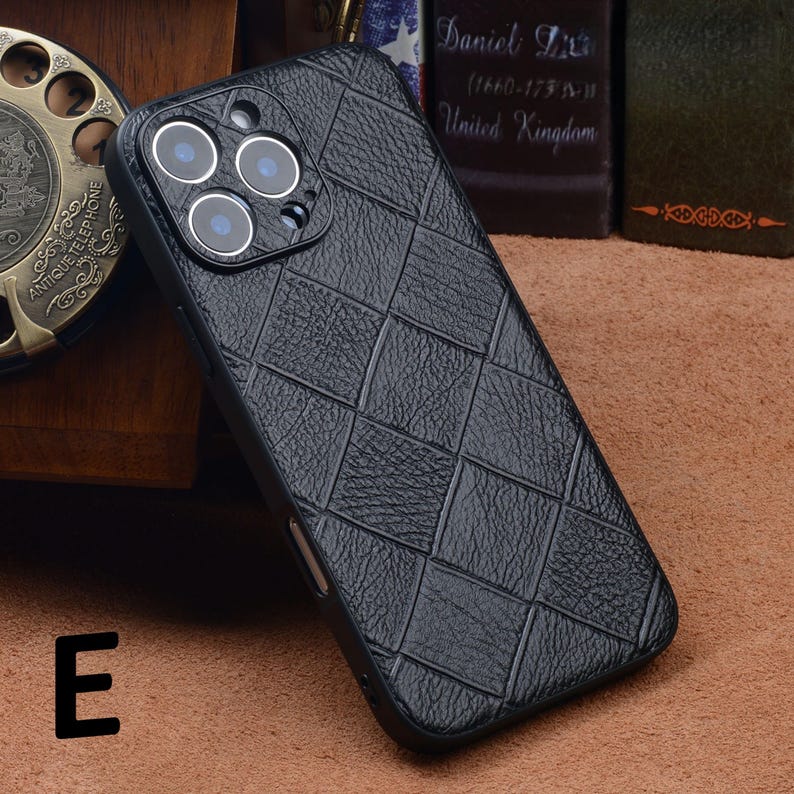 May include: Black phone case with a woven leather-like texture. The case has a square pattern and a camera module with three lenses. The letter "E" is visible in the lower left corner.