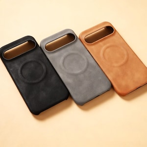 Op de afbeelding: Drie rechthoekige telefoonhoesjes in zwart, grijs en bruin. Elke hoes heeft een uitsparing voor de camera en een cirkelvormige inkeping op de achterkant. De hoesjes zijn gemaakt van een textuurrijk materiaal.