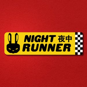May include: A rectangular yellow sticker featuring a black silhouette of a rabbit head on the left, the text NIGHT RUNNER and Japanese characters in black, and a black and white checkered pattern on the right edge against a red background.