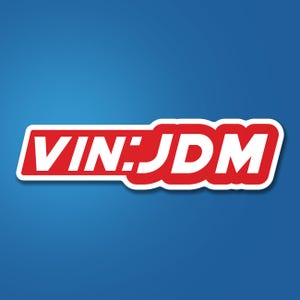 May include: A sticker with the text "VIN:JDM" in white, set against a red background with a white border. The sticker is on a blue background.