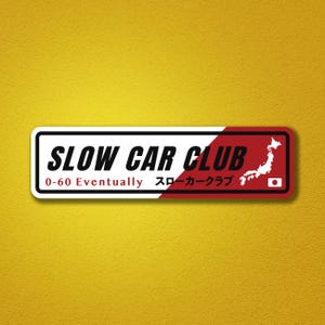 May include: A rectangular sticker featuring a white and red background with the black text SLOW CAR CLUB, the phrase 0-60 Eventually, Japanese text, a white silhouette map of Japan, and a small Japanese flag icon on the right side.
