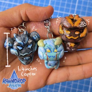 May include: Three sculpted character keychains with metal rings. One is dark blue with light blue accents, one is light blue with yellow eyes, and one is brown with orange markings. A white graphic indicates a height of approximately 1.4 inches.