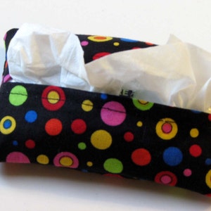 May include: A black fabric tissue box cover with colorful polka dots in red, yellow, green, blue, and pink. The tissue box cover is open and has white tissues inside.
