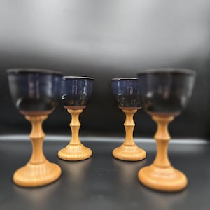 May include: Four handcrafted goblets with dark blue glazed bowls and light wood stems and bases. The goblets have a classic chalice shape, with a smooth, polished finish. The wood has a natural, warm tone.