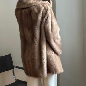 May include: A brown fur coat with a wide collar. The coat is knee-length and appears to be made of a soft, plush material. The coat is a neutral color and has a classic design.
