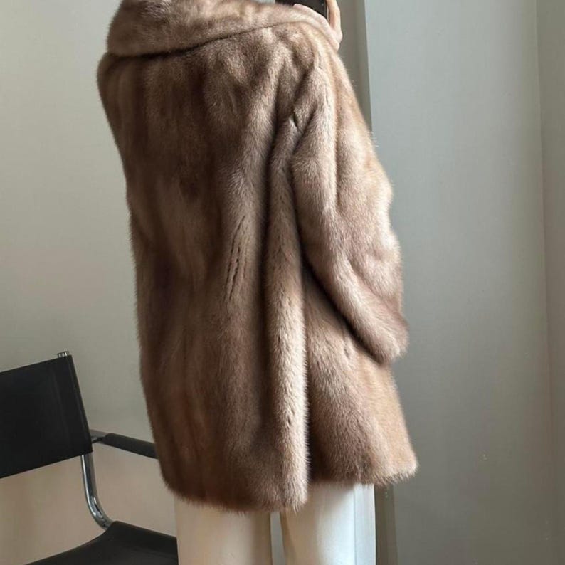 May include: A brown fur coat with a wide collar. The coat is knee-length and appears to be made of a soft, plush material. The coat is a neutral color and has a classic design.