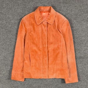 Peut inclure: Une veste en daim orange vif dot&eacute;e d'un col pointu classique, de manches longues et d'une patte de boutonnage avant dissimul&eacute;e. Le v&ecirc;tement pr&eacute;sente une coupe structur&eacute;e avec des coutures verticales sur les panneaux avant et deux poches.