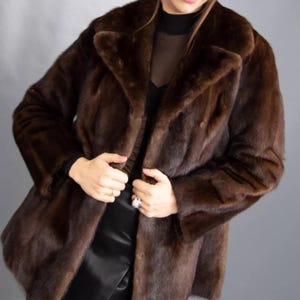 May include: A dark brown fur coat with a traditional collar and long sleeves. The coat is a deep brown shade and looks to be made of soft fur. The coat is fastened and has a tailored fit.