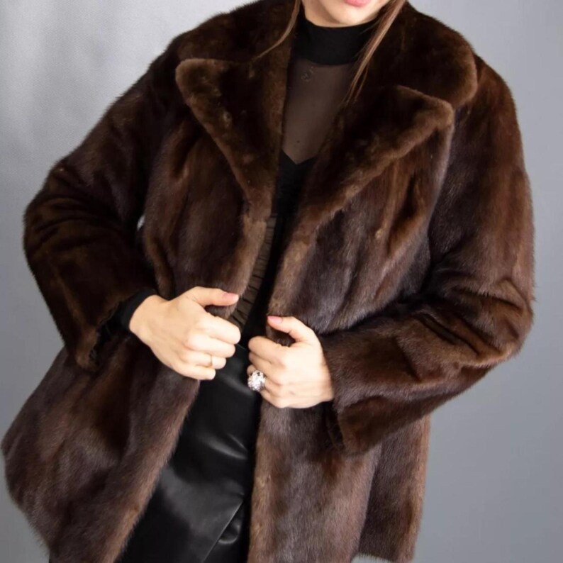 May include: A dark brown fur coat with a traditional collar and long sleeves. The coat is a deep brown shade and looks to be made of soft fur. The coat is fastened and has a tailored fit.