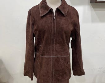 May include: A brown suede jacket with a zip-up front and a collared neckline. The jacket has white stitching along the seams and around the collar. The jacket is displayed on a wooden mannequin.