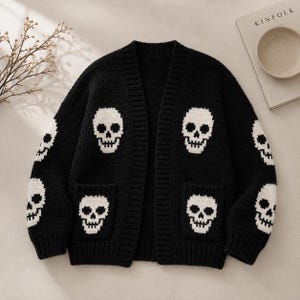 Könnte beinhalten: Eine schwarze Langarm-Strickjacke mit einem sich wiederholenden weißen Totenkopfmuster auf der Vorderseite, den Ärmeln und den zwei Vordertaschen. Das Kleidungsstück hat einen V-Ausschnitt, gerippte Bündchen und einen gerippten Saum.