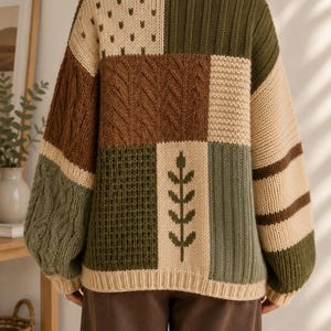 Peut inclure: Un pull &agrave; manches longues pr&eacute;sentant un motif patchwork dans des tons vert olive, cr&egrave;me et marron. Le v&ecirc;tement en tricot affiche diverses textures, notamment des torsades, des motifs c&ocirc;tel&eacute;s et un motif de feuille central au dos.