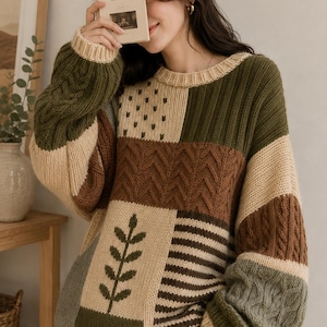 Peut inclure: Un pull en tricot &agrave; manches longues avec un motif patchwork dans des tons vert olive, cr&egrave;me et marron. Le pull pr&eacute;sente diverses textures, notamment des torsades, des c&ocirc;tes et un motif de feuille. Le livre tenu indique CAFE DE FLORE.