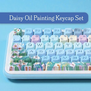 以下が含まれることがあります： 白枠とキーキャップが付いた水色のキーボード。キーキャップは水色で白い文字で、デイジーの油絵のデザインが施されています。「Daisy Oil Painting Keycap Set」というテキストが青いバナーに表示されています。
