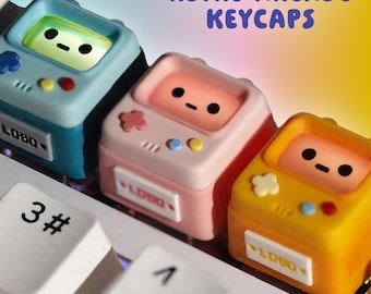 May include: Three colorful retro arcade keycaps in blue, pink, and yellow, each with a small screen and a cute face. The keycaps are on a white keyboard, with the text "RETRO ARCADE KEYCAPS" in purple.