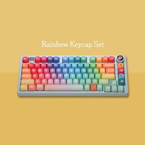 以下が含まれることがあります： 虹色のキーキャップが付いたフルサイズのキーボード。キーは赤から紫まで虹の色を通過します。キーボードは明るい灰色のフレームで、「Rainbow Keycap Set」というテキストが上にあります。