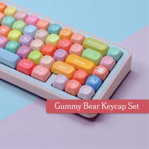 Può includere: Una tastiera con tasti multicolori dai colori pastello. I tasti sono nelle tonalità del rosa, giallo, verde, blu e arancione. La tastiera ha una cornice azzurra e il testo "Gummy Bear Keycap Set" è visualizzato su uno striscione rosso.