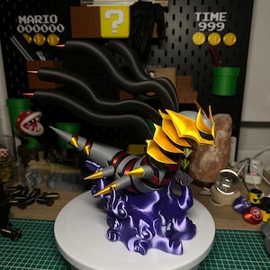 Pode incluir: Uma figura detalhada impressa em 3D de uma criatura serpentina com cabeça amarela e preta, corpo cinza e detalhes vermelhos, pousada sobre uma base de nuvem roxa. O fundo apresenta um painel preto com elementos temáticos do Mario e o texto "TIME 999".