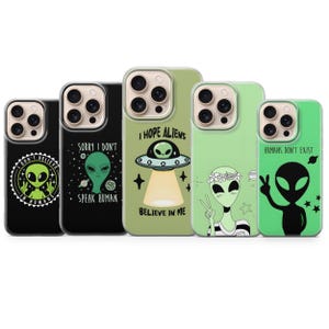 May include: Five phone cases featuring alien-themed graphics. The designs include green aliens, UFOs, and text such as I DON'T BELIEVE IN HUMANS, SORRY I DON'T SPEAK HUMAN, I HOPE ALIENS BELIEVE IN ME, and HUMANS DON'T EXIST, set against black and green backgrounds.