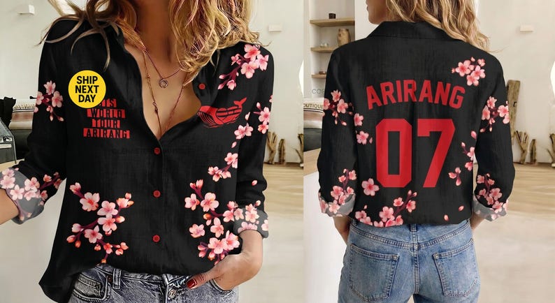 May include: A black long-sleeve button-down shirt featuring a pink cherry blossom floral pattern. The front displays the text "ITS WORLD TOUR ARIRANG" and a small red graphic. The back features the red text "ARIRANG" above the large red number "07".