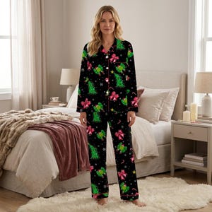May include: A black long-sleeve button-down pajama set featuring a festive holiday print with green Christmas trees, bright pink bows, and small white snowflakes. The pajamas have a classic collar, a front button closure, and long matching pants.