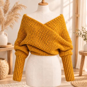 May include: A mustard yellow long-sleeve sweater featuring a textured knit pattern, a deep V-neckline, and a wrap-style front design. The garment has long, ribbed cuffs and a cropped length, displayed on a neutral-toned mannequin torso.