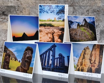 May include: A collection of six photographic prints featuring iconic landmarks and landscapes. The images include pyramids at sunset, ancient ruins, and statues. Each print is displayed on a white stand, with the artist's signature at the bottom.
